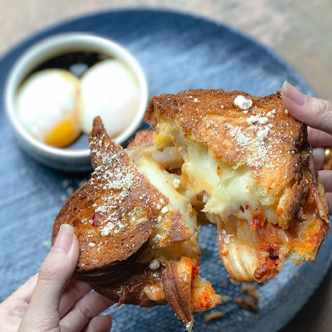 Kimchi toastie [$19] House cured bacon, mozzarella, orange cheddar, kimchi sandwiched in a danish loaf toasted to crispness, served with a side of onsen eggs.